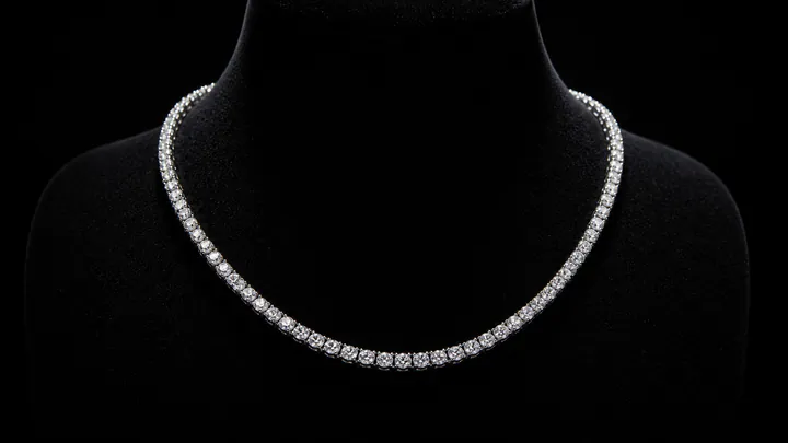A diamond tennis necklace catches overhead light against a dark velvet display.
